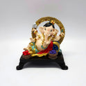 Front view of a 16cm hand-painted reclining Ganesha resin statue on a dark throne base with fruit bowls by Sri Swaminathan and Co