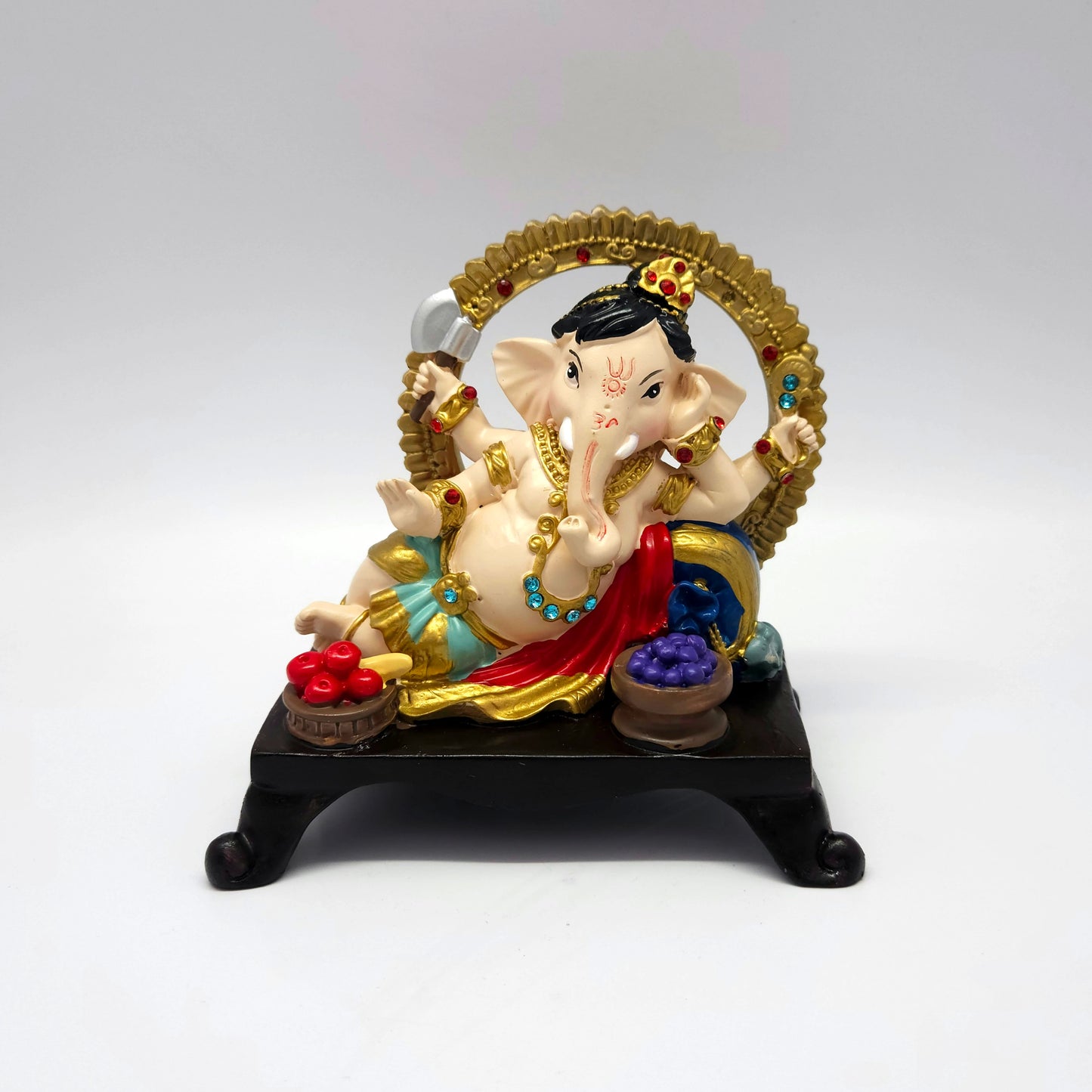 Front view of a 16cm hand-painted reclining Ganesha resin statue on a dark throne base with fruit bowls by Sri Swaminathan and Co