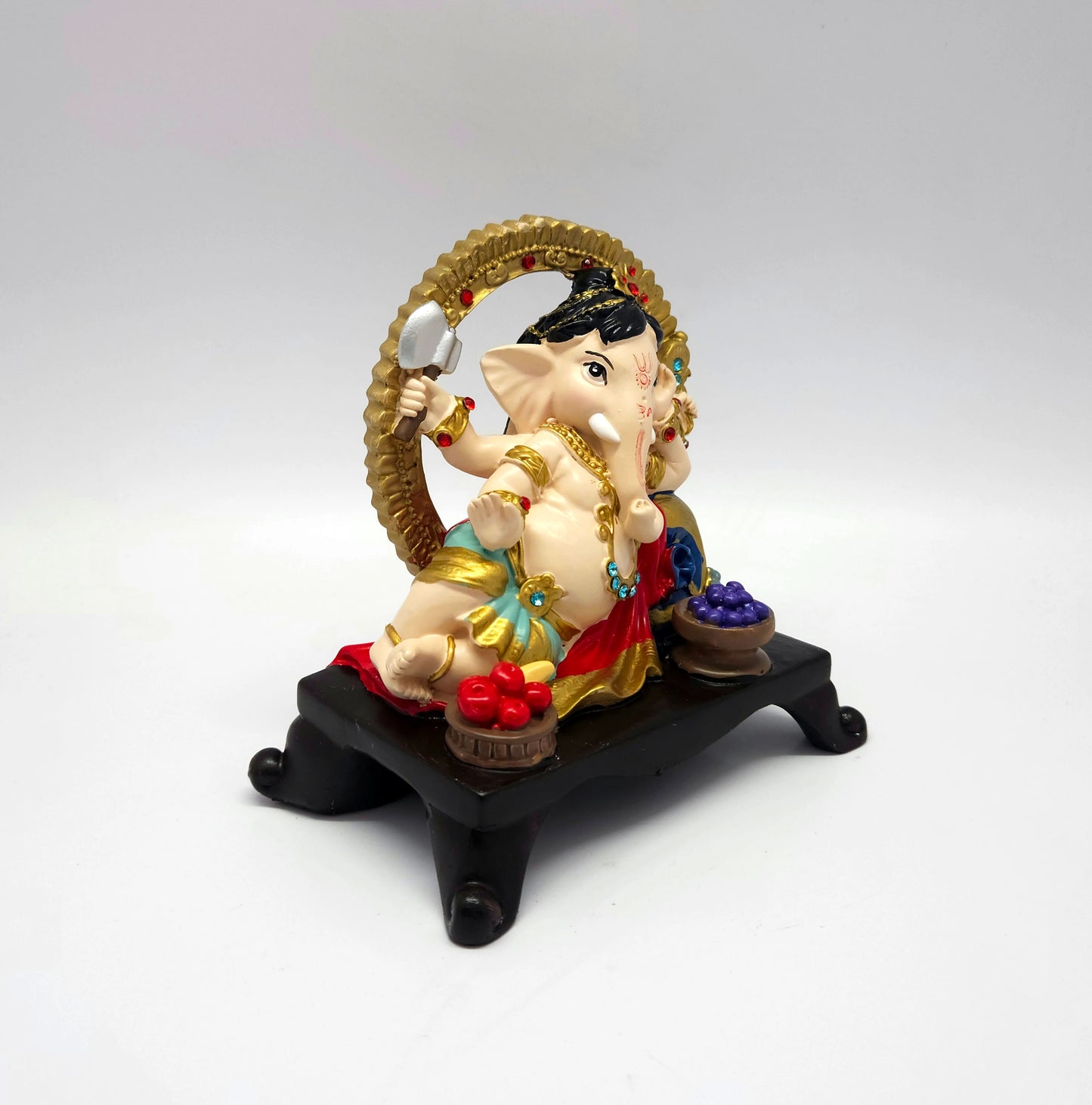 Three-quarter perspective of a multi-color resin Ganpati statue highlighting the gold halo and blue rhinestone placements.