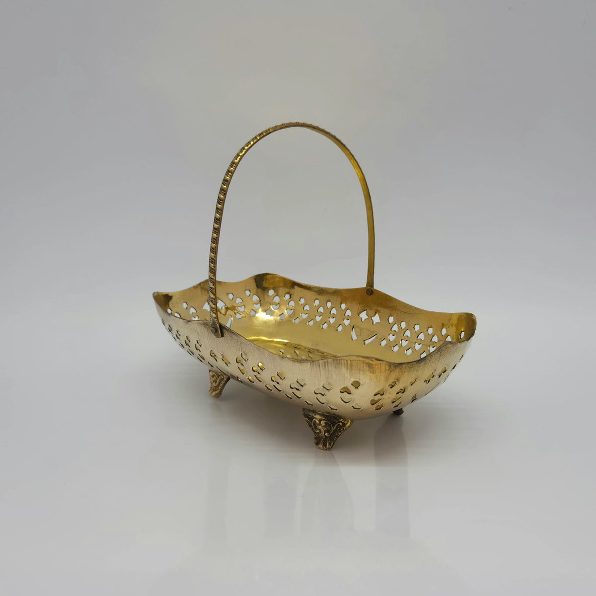 Three-quarter front perspective view of the 17.5cm jali cutwork brass pooja carrier basket showcasing its upright handle and four sturdy support legs.
