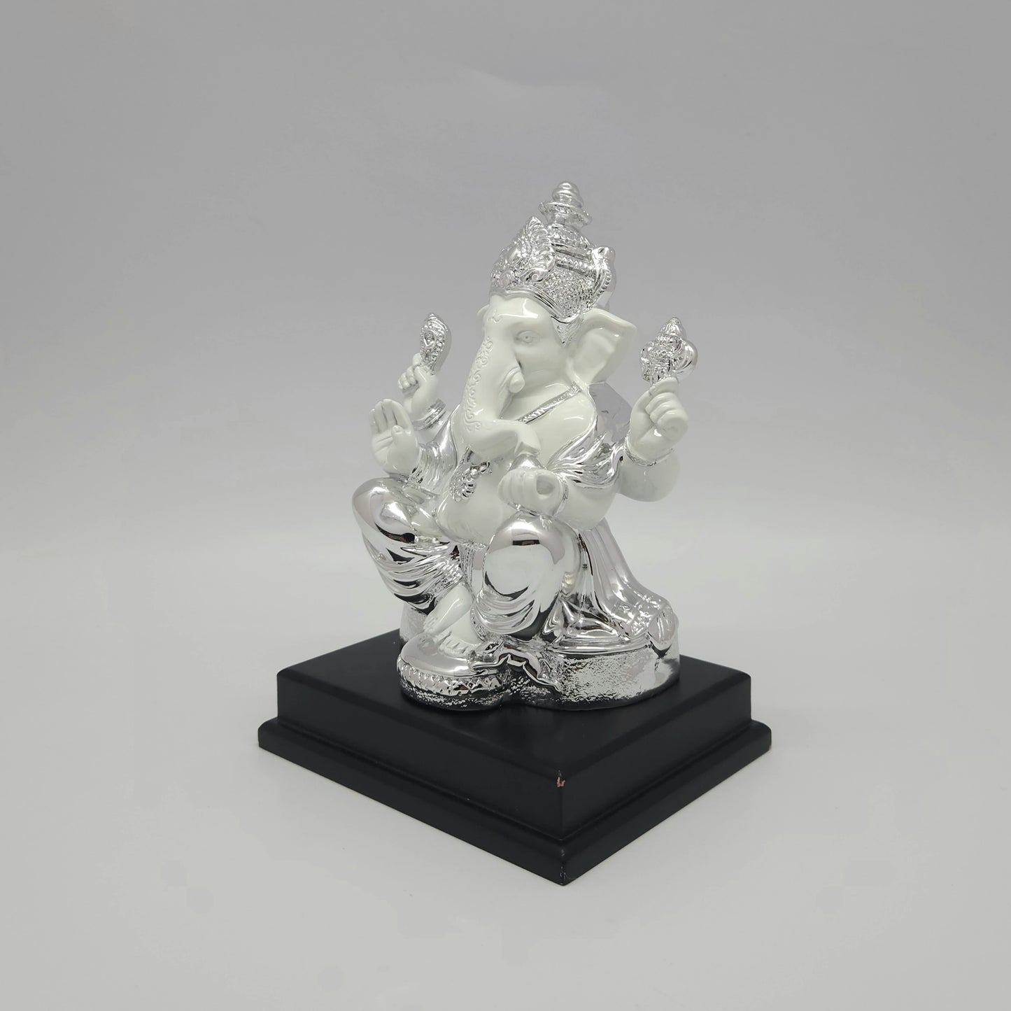 Left three-quarter angle view of the silver electroplated resin Ganpati idol showcasing the thick square dark pedestal stand.