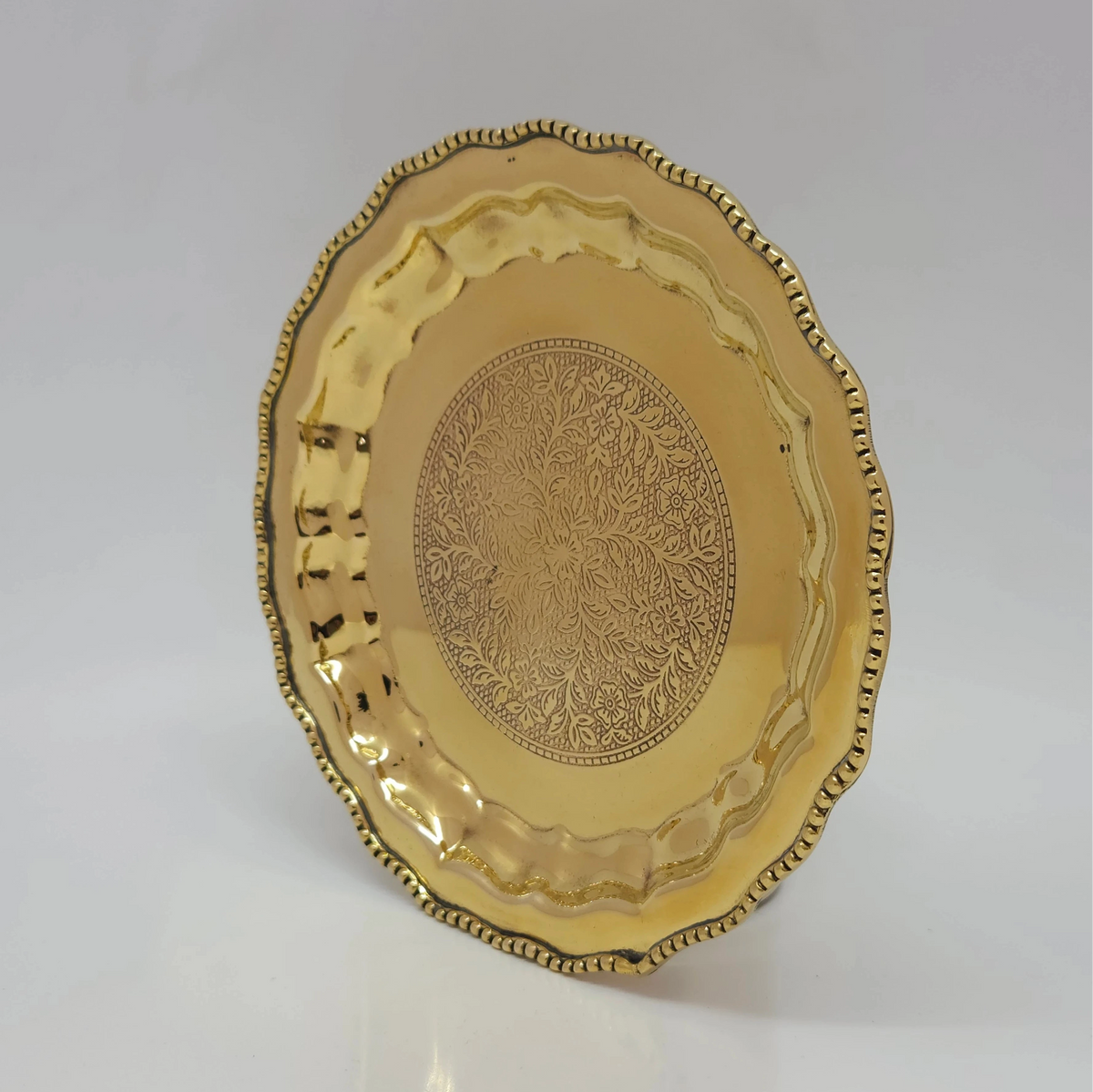 Side tilting profile view of the six inch brass pebble engraved thamboolam plate demonstrating the shallow basin depth and hand-polished golden mirror luster