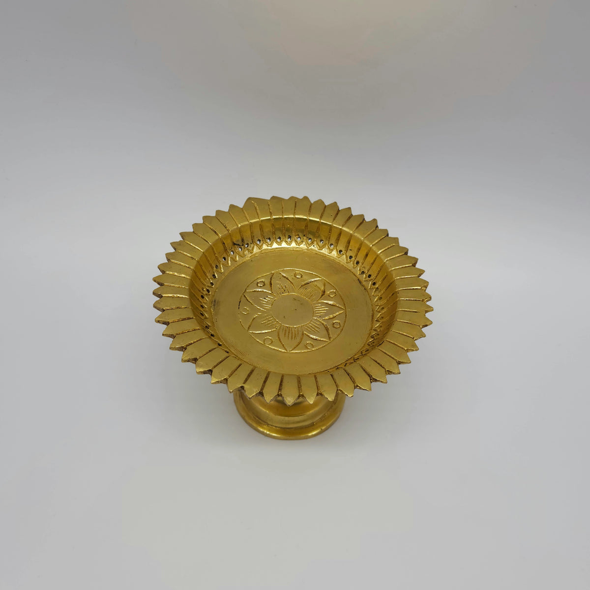 High angle tilted view of the premium brass pooja stand showcasing the detailed ridge lines carved along the outer rim border.