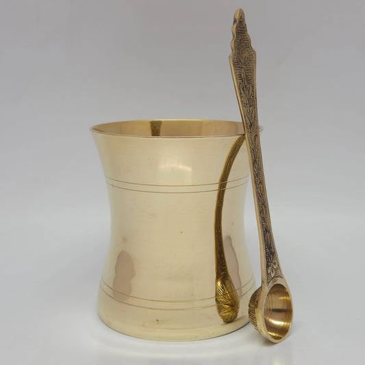 Straight front view of the ten point five centimeter large brass panchapathram cup shown with the sixteen point five centimeter long uthirani spoon standing upright outside the vessel
