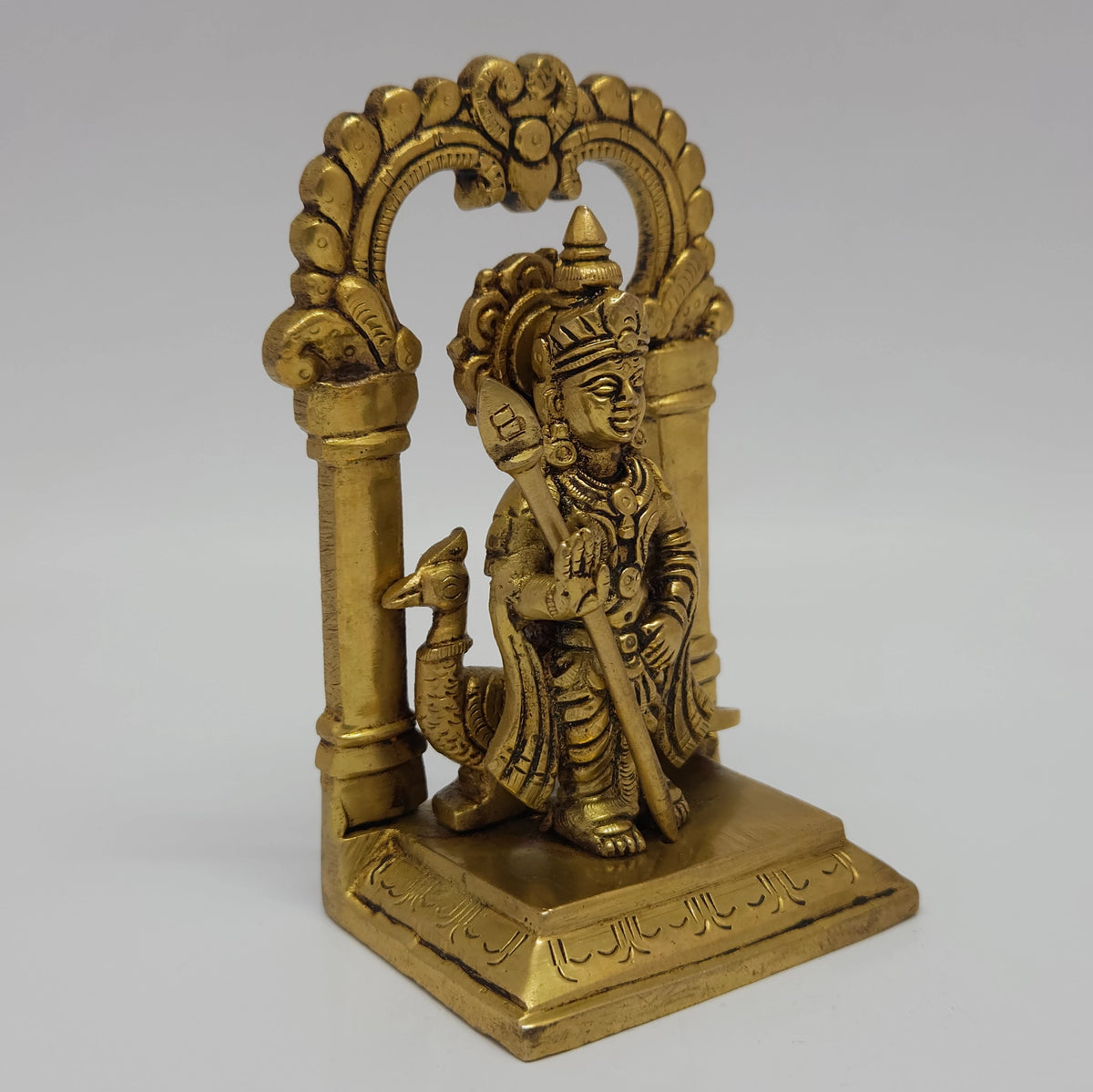 Three-quarter front left perspective view of the twelve point five centimeter brass Karthikeyan statue highlighting the smooth temple pillar lines and square throne base