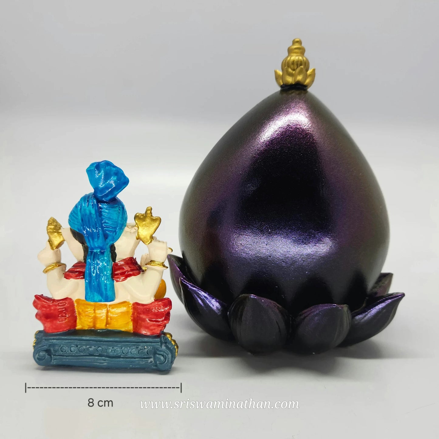 Rear view of the blue turban Ganesha idol placed next to the empty metallic purple leaf canopy frame with gold top finial.
