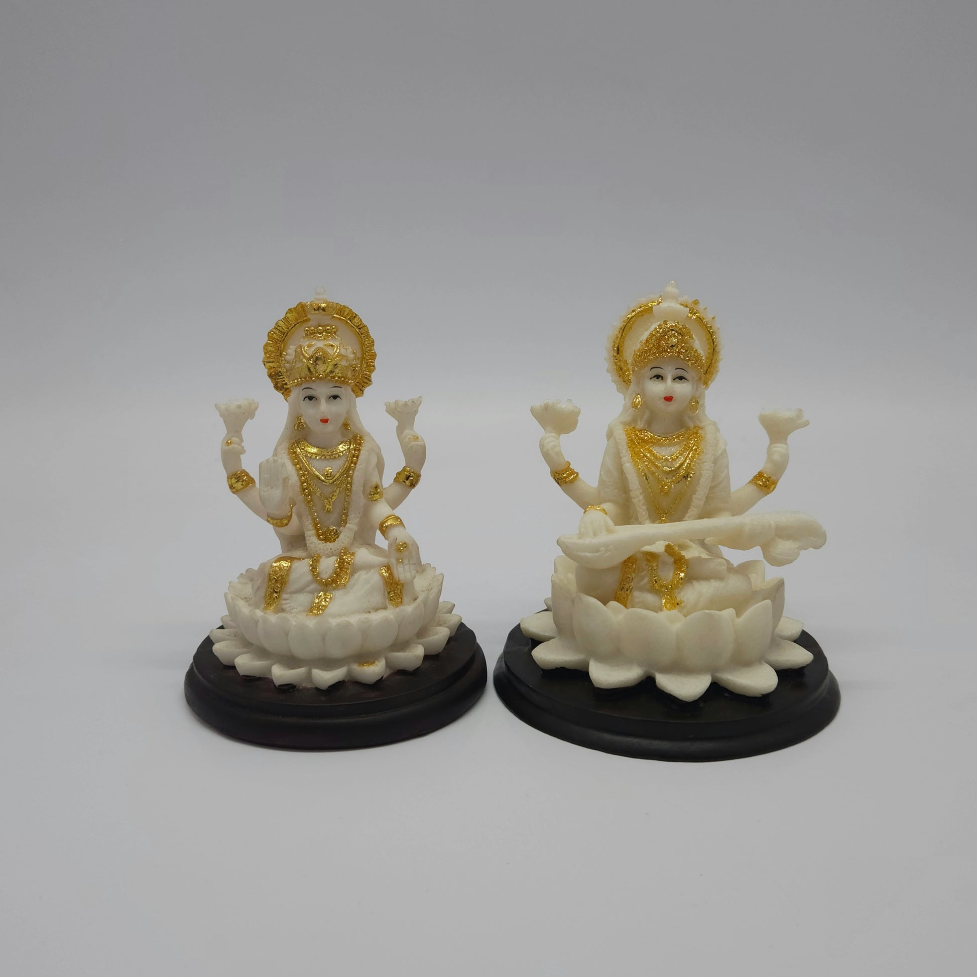Showcase view of the white poly-marble resin Goddess Lakshmi statue placed side-by-side with a matching style matching idol on a dark base for festive pooja setups.