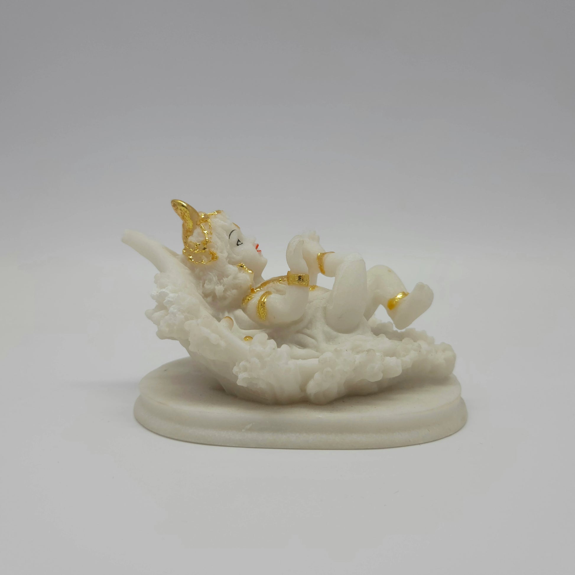 Front left view of a 7.5cm white marble-finish resin baby Krishna statue reclining on a sacred leaf by Sri Swaminathan and Co.