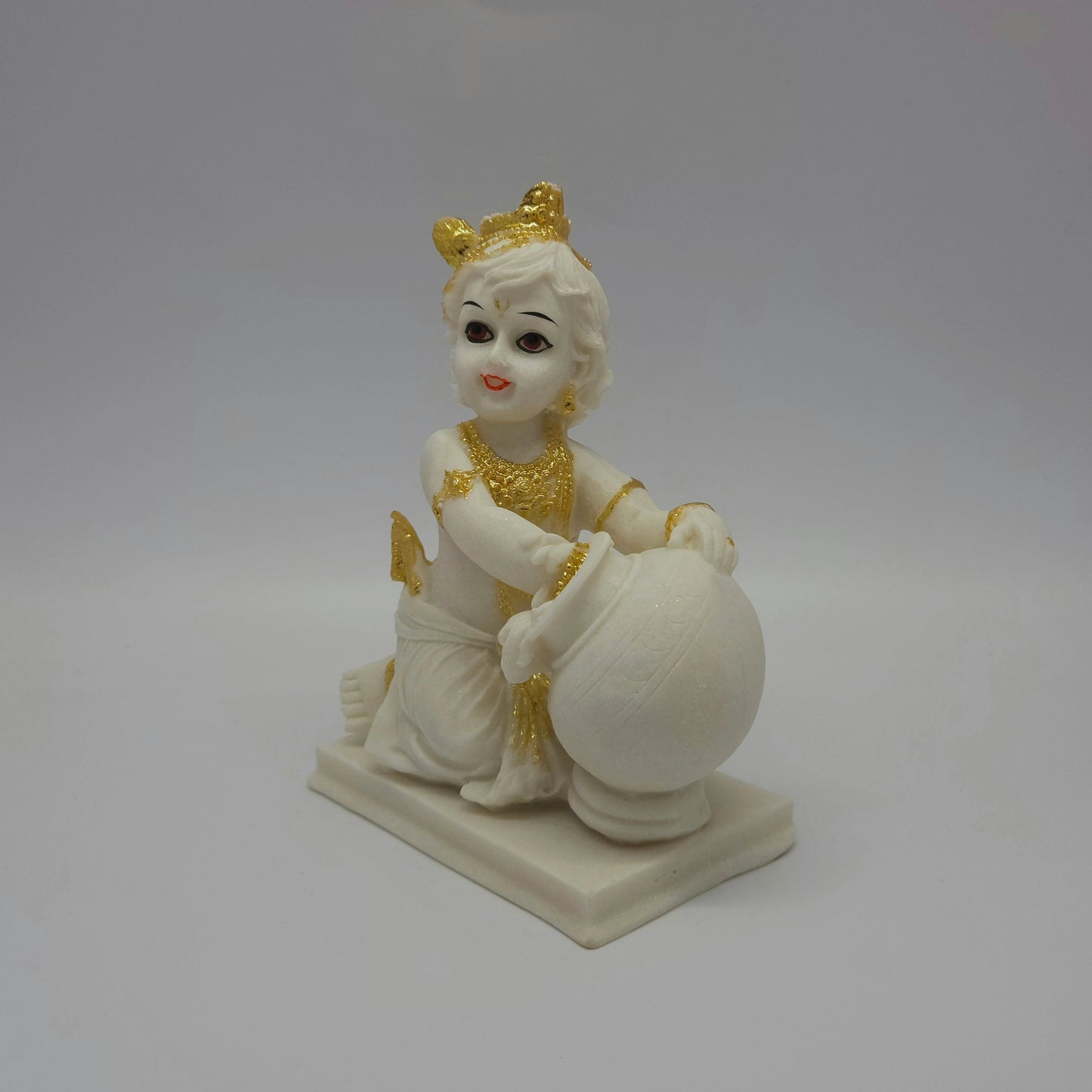 Three-quarter left angle view of an 18cm white marble-finish resin baby Krishna statue kneeling beside an overflowing butter pot by Sri Swaminathan and Co