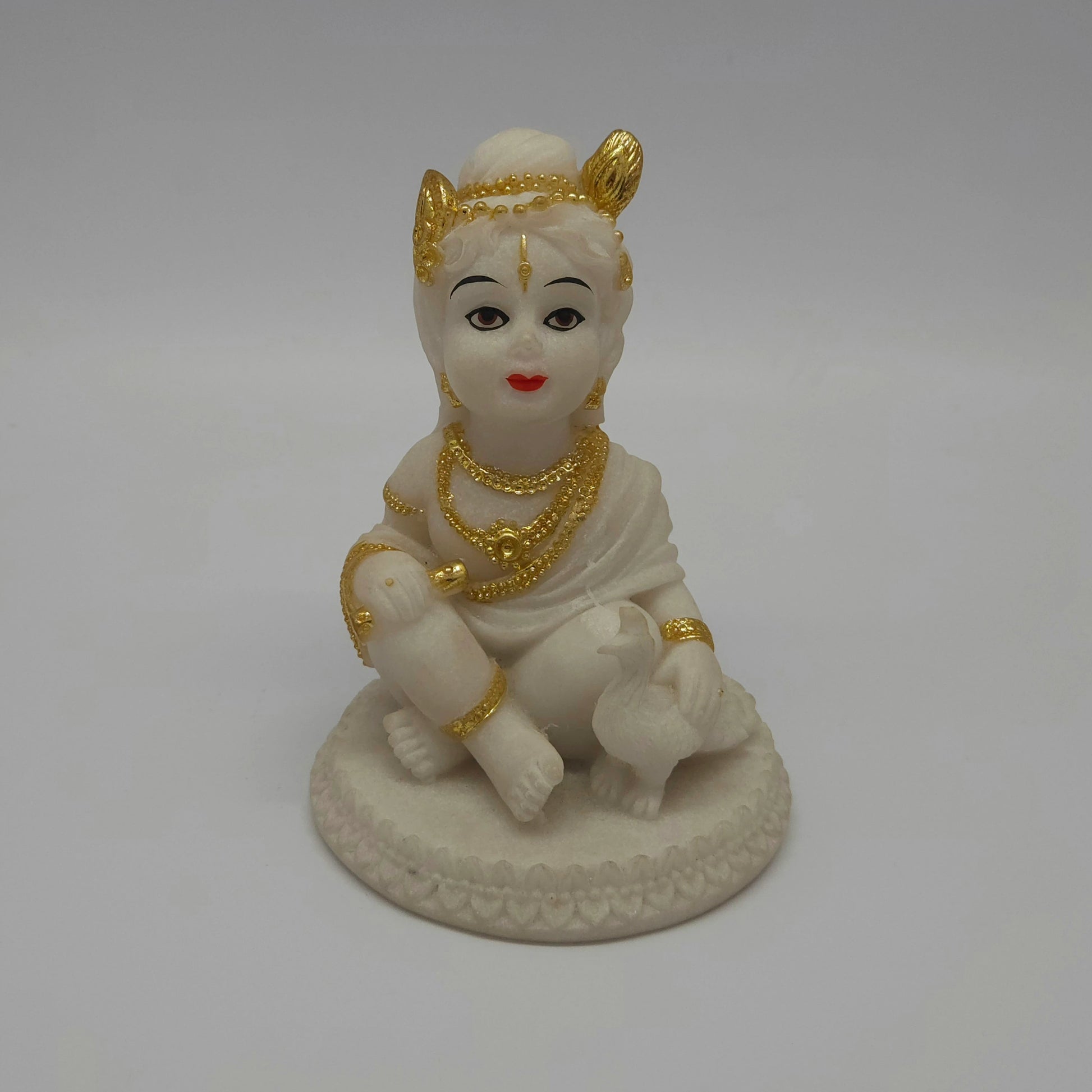 Front view of a 12.5cm white marble-finish resin baby Krishna statue sitting on a circular lotus base with a peacock by Sri Swaminathan and Co.