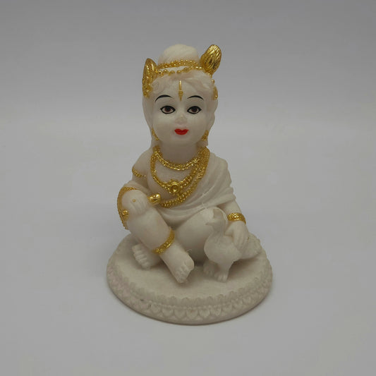 Front view of a 12.5cm white marble-finish resin baby Krishna statue sitting on a circular lotus base with a peacock by Sri Swaminathan and Co.