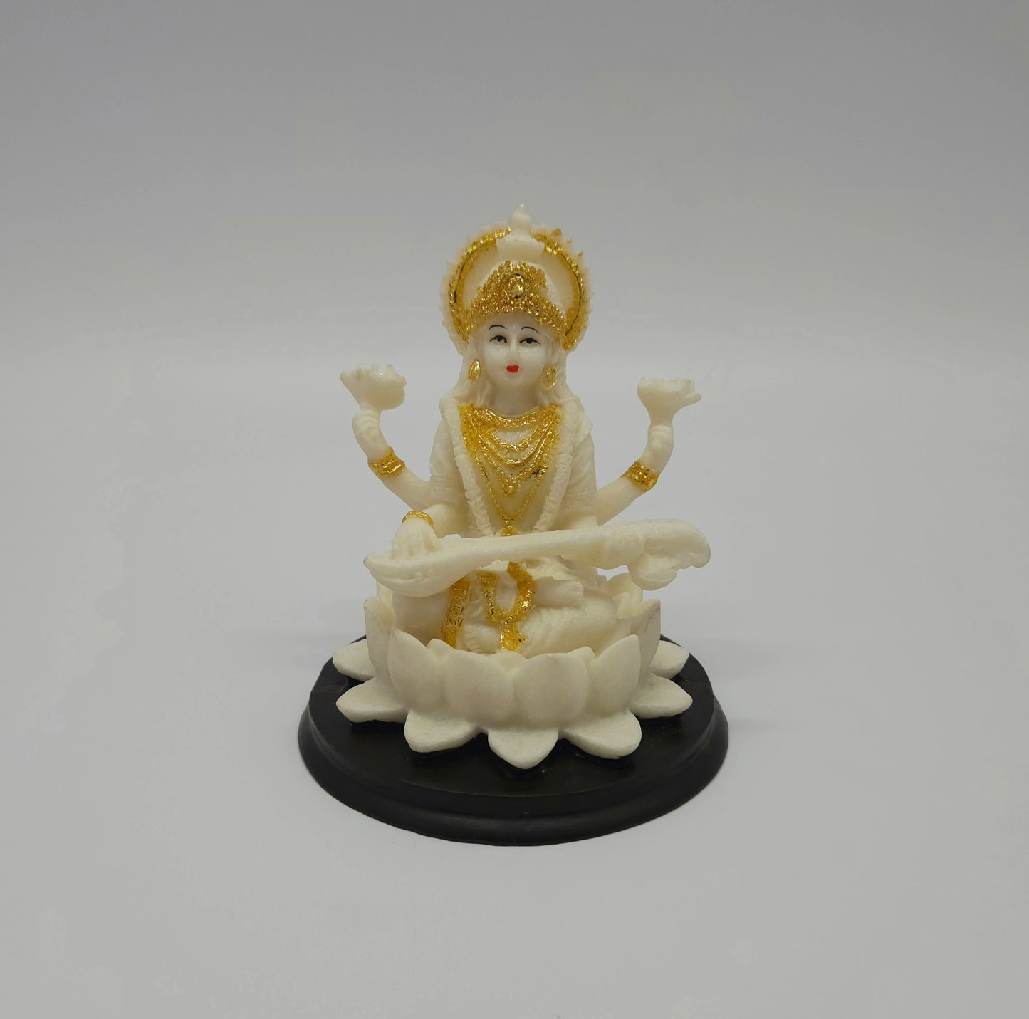 Front view of a 10.5cm white marble-finish resin Goddess Saraswati statue playing a veena on a circular black base by Sri Swaminathan and Co.