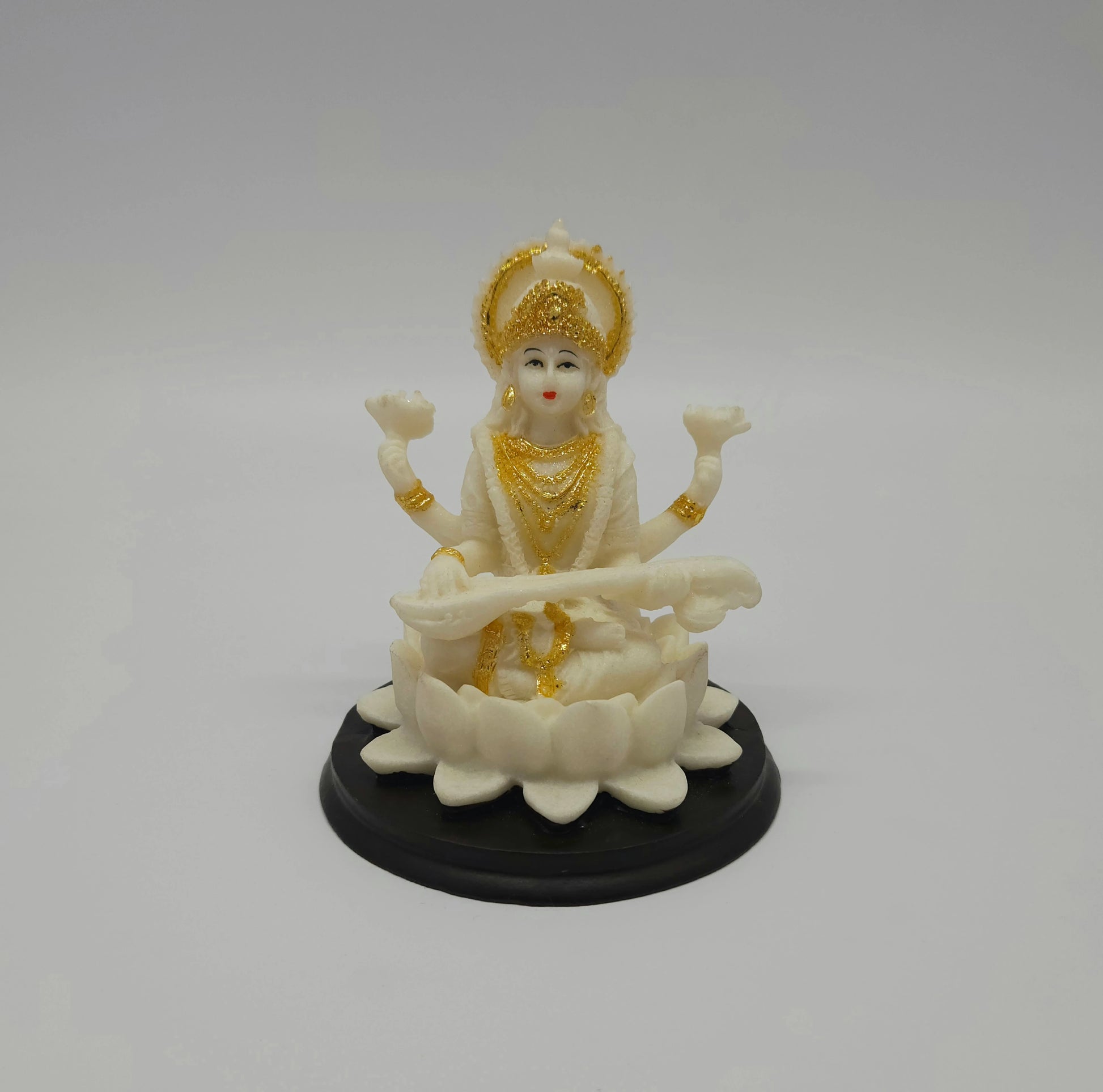 Front view of a 10.5cm white marble-finish resin Goddess Saraswati statue playing a veena on a circular black base by Sri Swaminathan and Co.