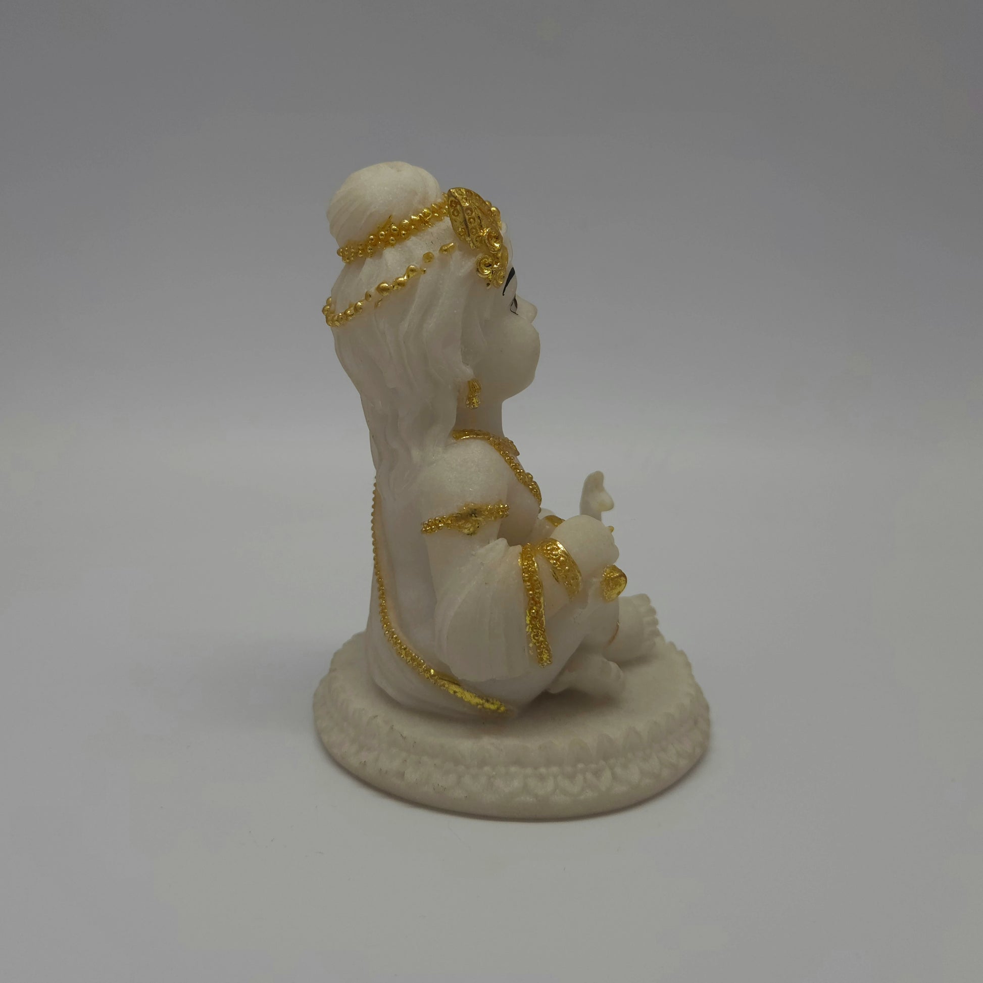 Left side profile view of the white marble texture resin baby Krishna idol showing the thickness of the circular base and his seated depth.