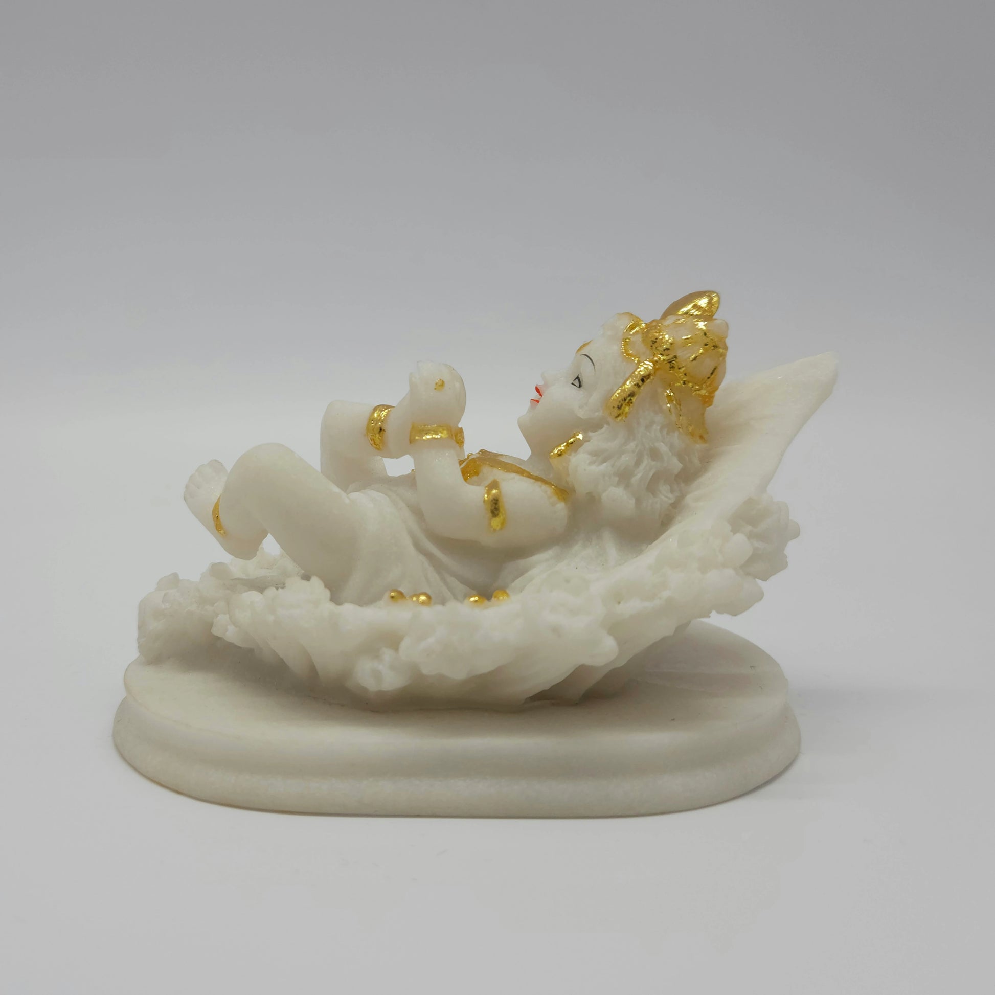 Straight side view of the white resin baby Krishna idol resting on his back and raising his foot playfully.