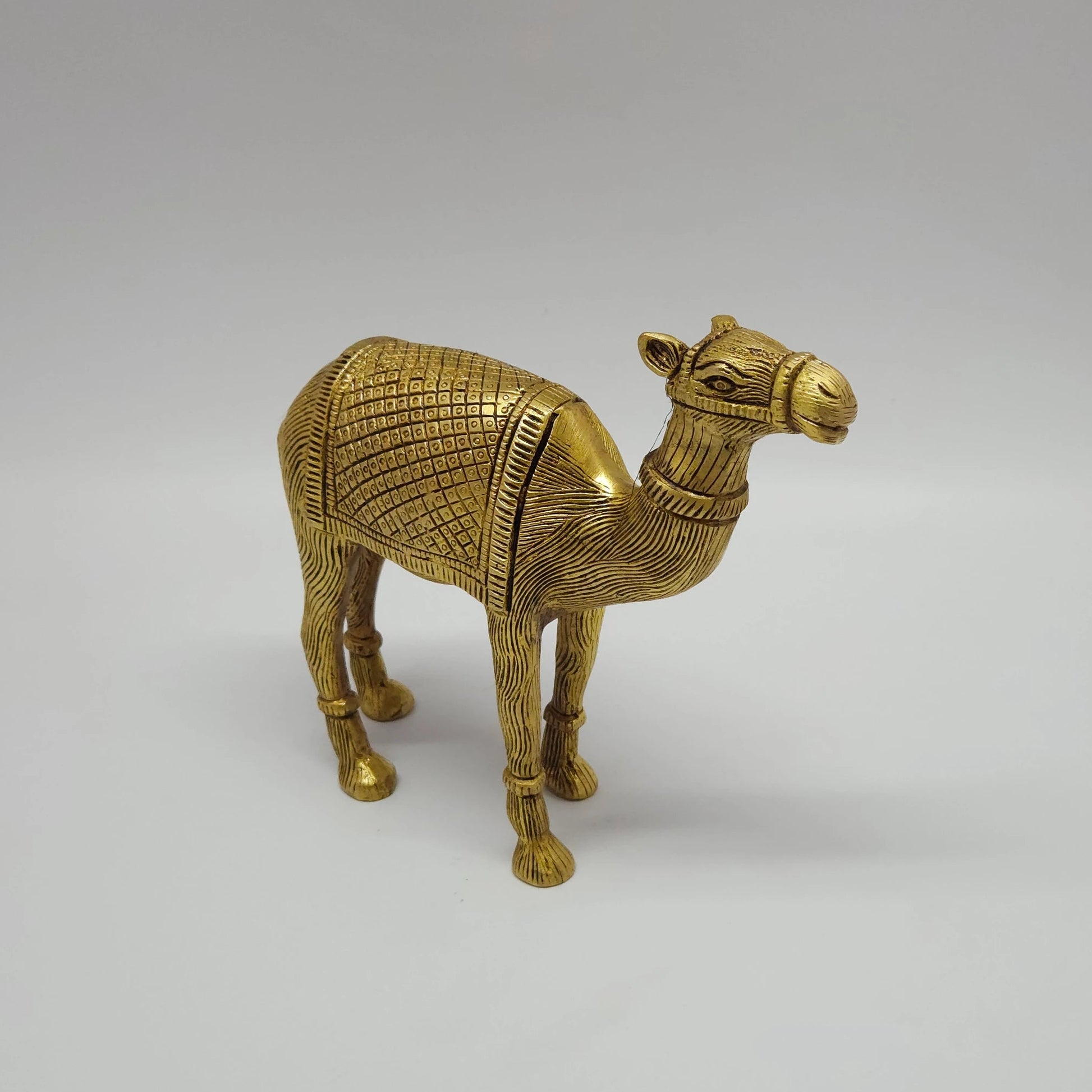 Sri Swaminathan and Co brass standing camel showpiece antique finish 20cm length 45 degree right pose corner view focusing on the deep etched geometric grid saddle blanket and base footprint