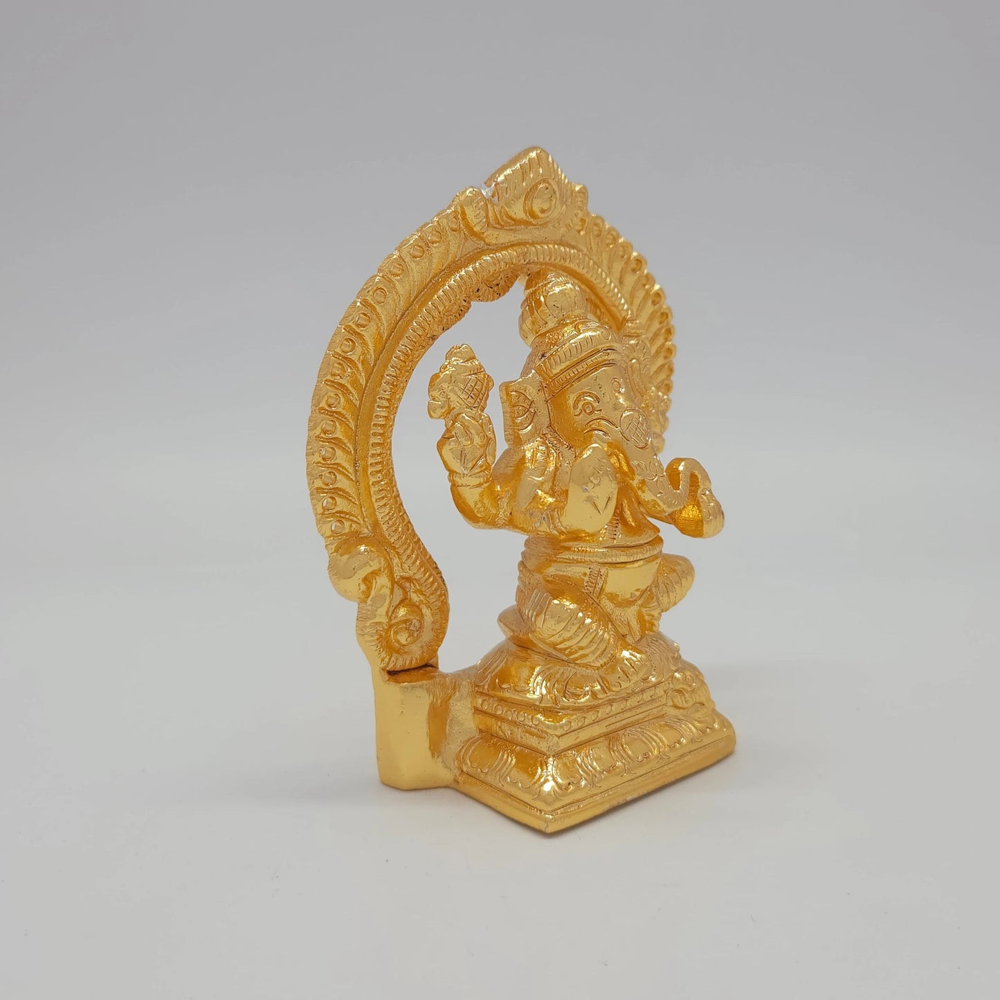 Sri Swaminathan and Co brass miniature Chaturbuja Ganapathi statue gold finish 250g weight 45 degree right pose corner view focusing on protective abhaya mudra hand and rectangular base depth