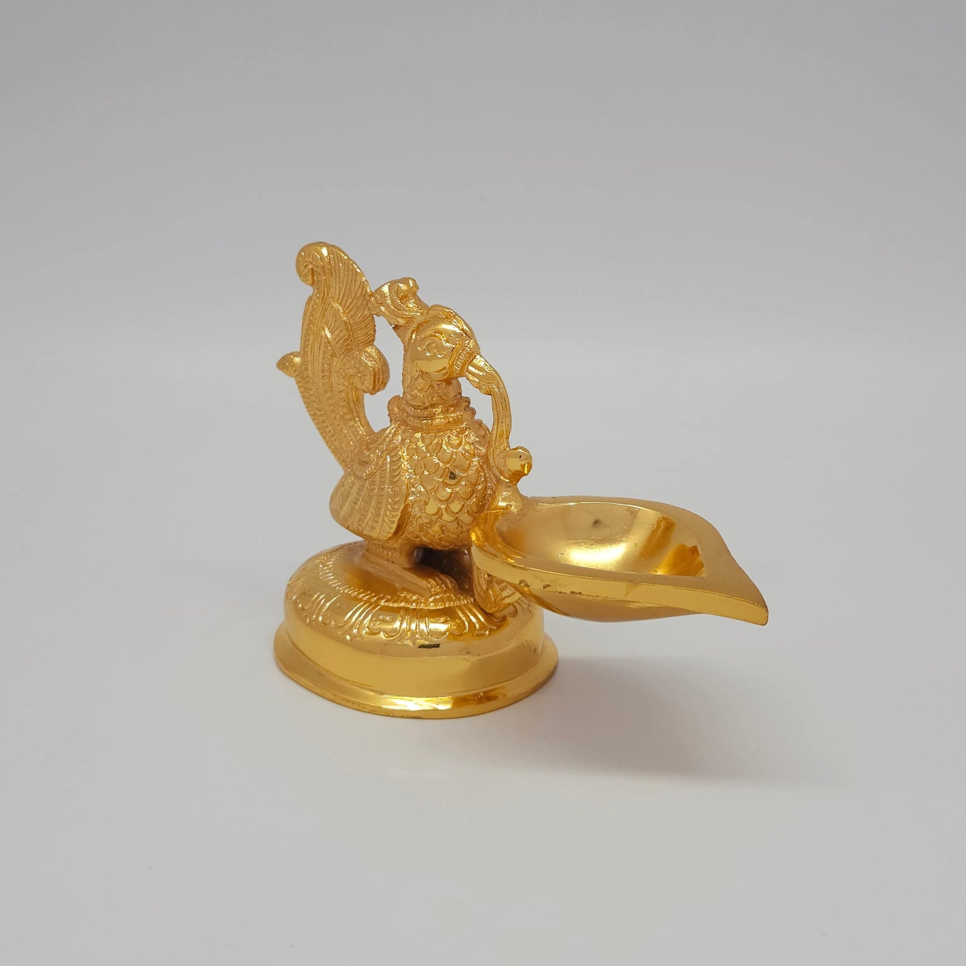 Sri Swaminathan and Co brass decorative peacock showpiece gold finish 610g 45 degree right pose corner view focusing on smooth single wick style lamp reservoir and base depth