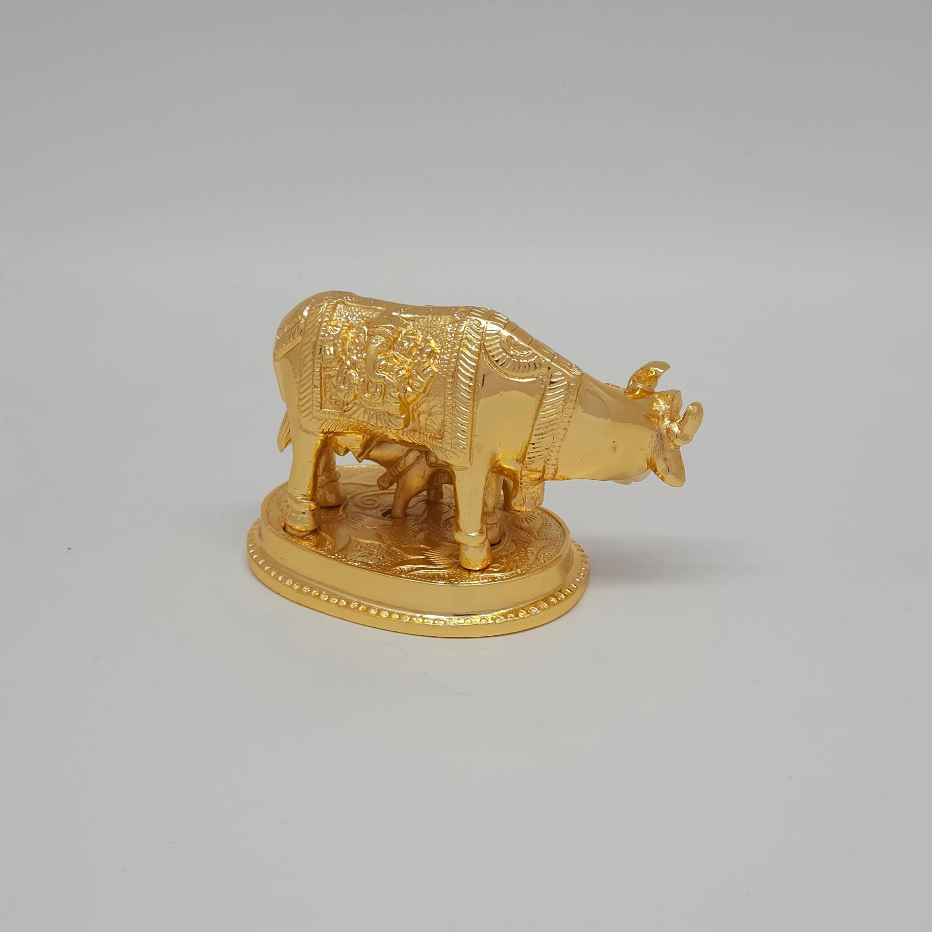 Sri Swaminathan and Co pure brass Kamadhenu cow and calf statue gold powder coated 7cm height 45 degree angle focusing on the embossed Lord Ganesha side blanket detail