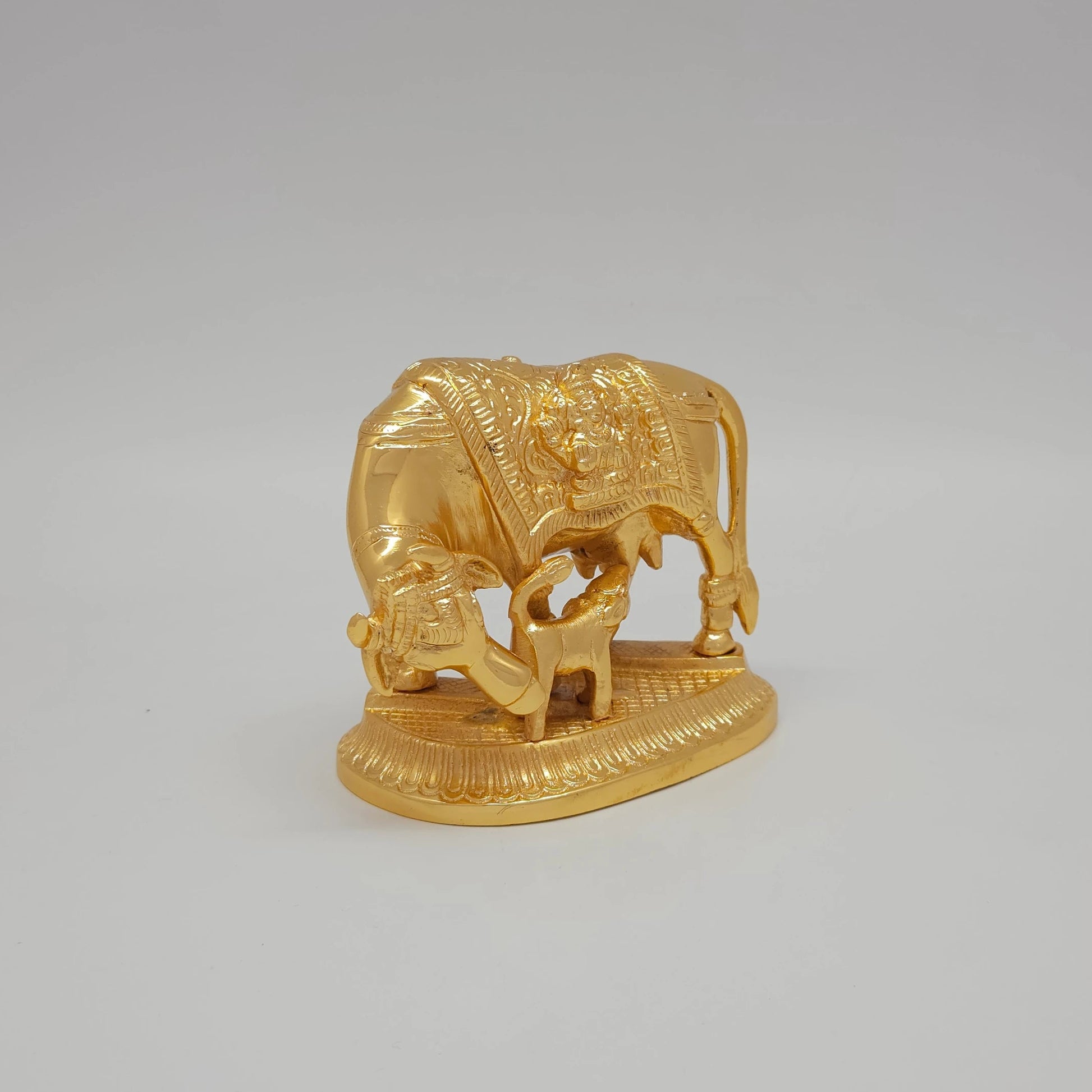 Sri Swaminathan and Co pure brass Kamadhenu cow and calf statue gold powder coated 9cm height 45 degree left pose corner view focusing on the calf drinking milk and base texture