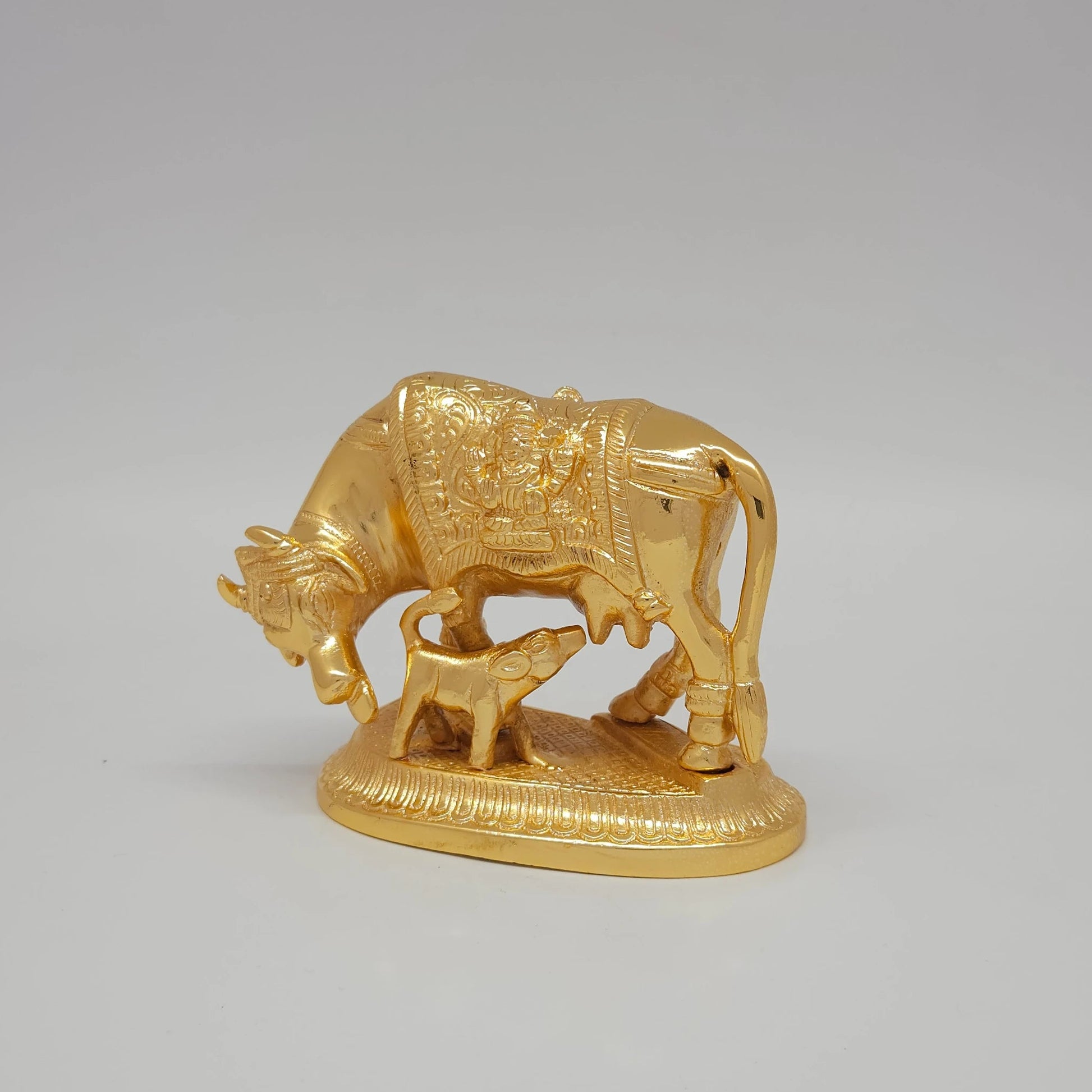 Sri Swaminathan and Co pure brass Kamadhenu cow and calf statue gold powder coated 9cm height 45 degree left pose corner view highlighting the chiseled deity back blanket detail