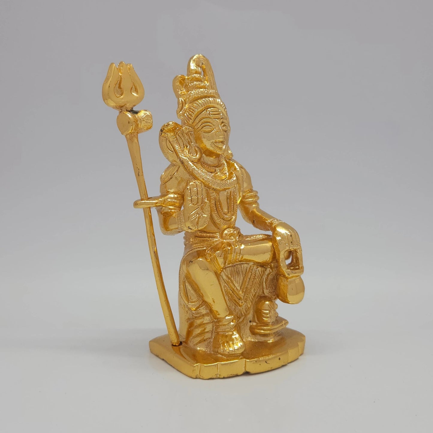 Sri Swaminathan and Co brass miniature seated Shiva statue gold finish 750g weight 45 degree left pose corner view highlighting the freestanding trishula trident shaft and damaru drum details
