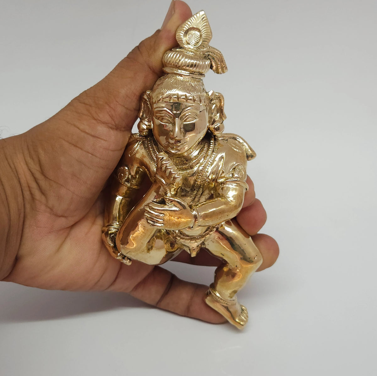 Handheld vertical close-up view focusing on the hand-chiseled features of the crown and face on the 6.5 inch Panchaloha Baby Krishna statue.
