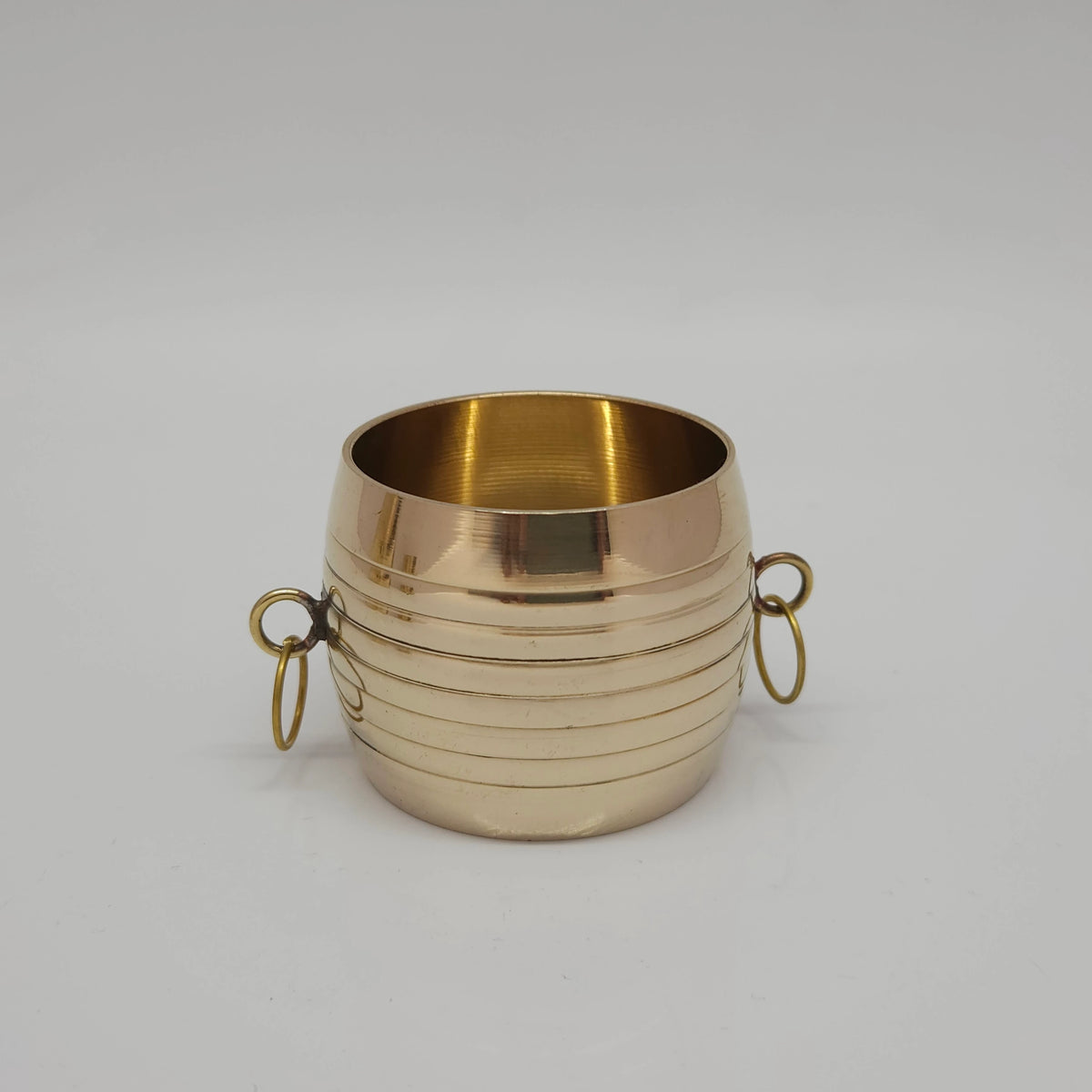 Standalone front profile shot of a traditional pure brass padi measuring vessel showing detailed concentric grooves and side drop rings.
