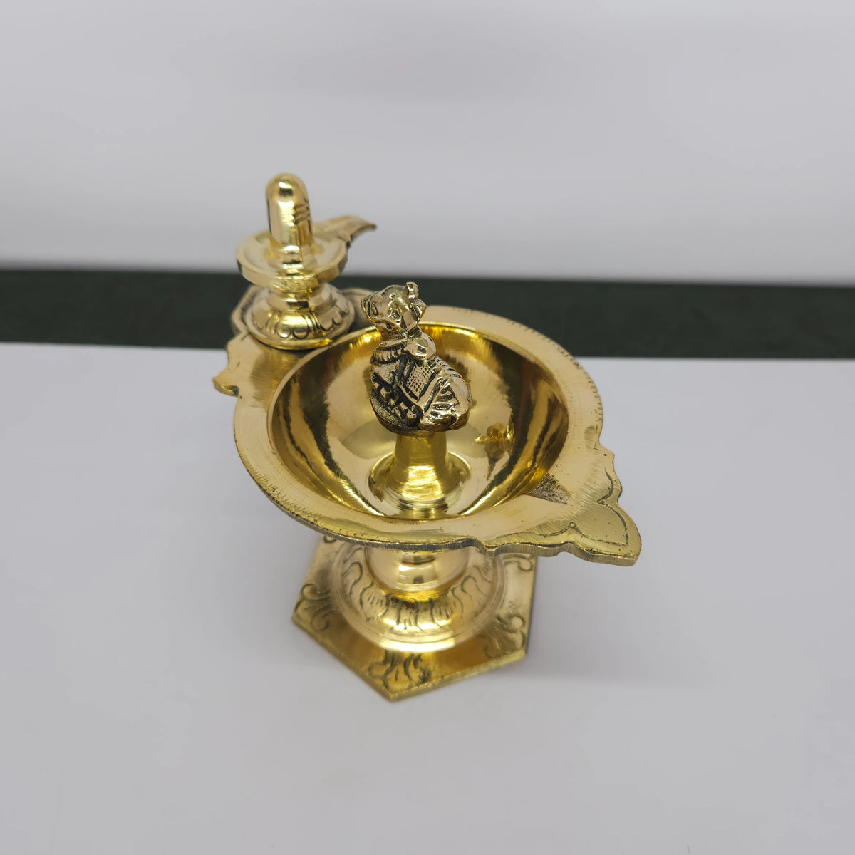 Three-quarter angle view of a solid brass Shiva Lingam and Nandi pedestal oil lamp, highlighting the polished golden mirror finish.
